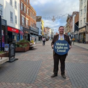 Alex McIntyre MP standing on Westgate Street holding a Shine a Light on Local bauble.